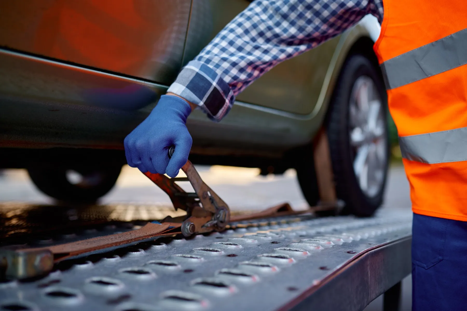 A transport worker ratcheting a strap over a car's wheel on a trailer