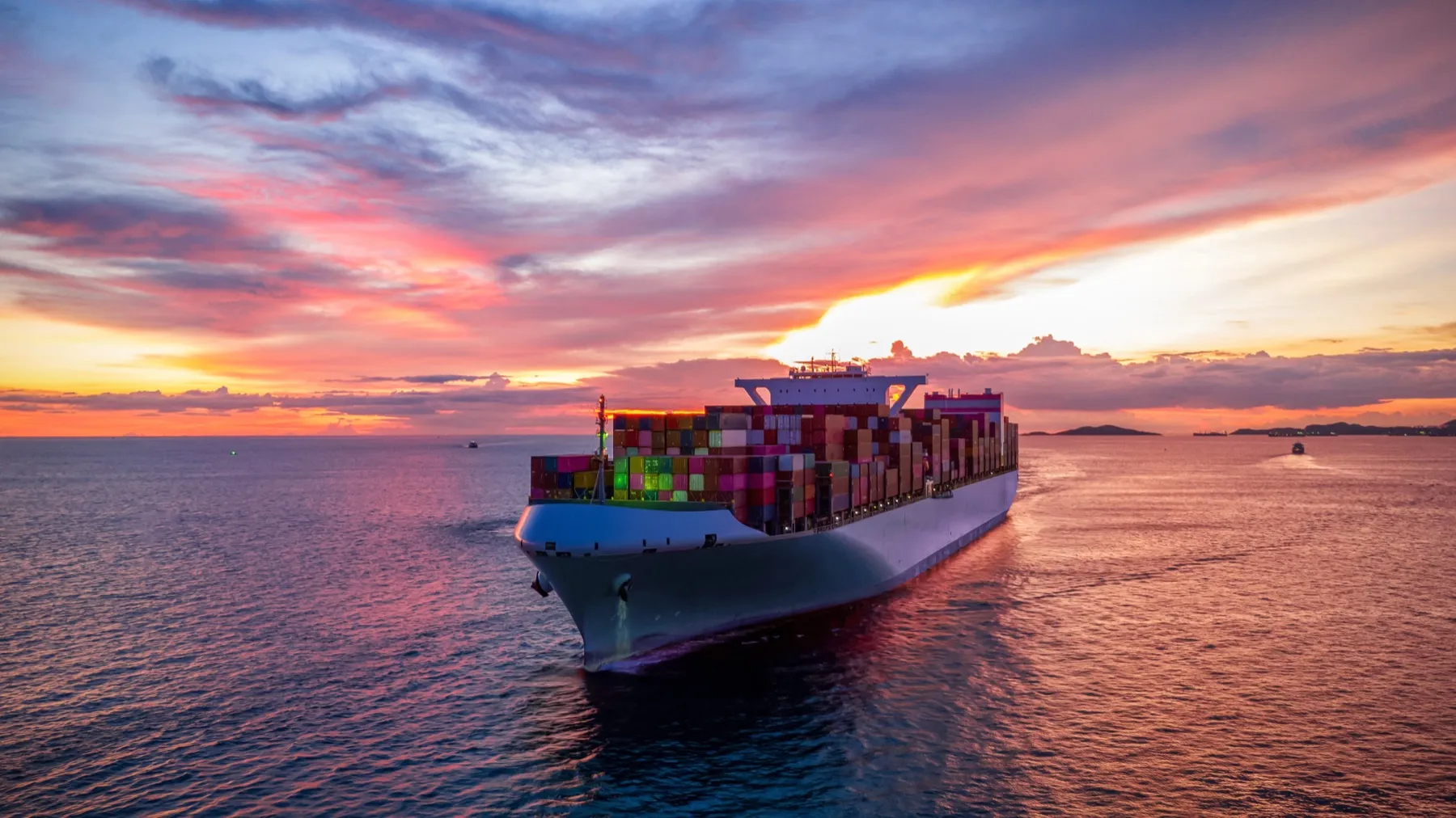 A loaded container ship heading out to sea at sunset