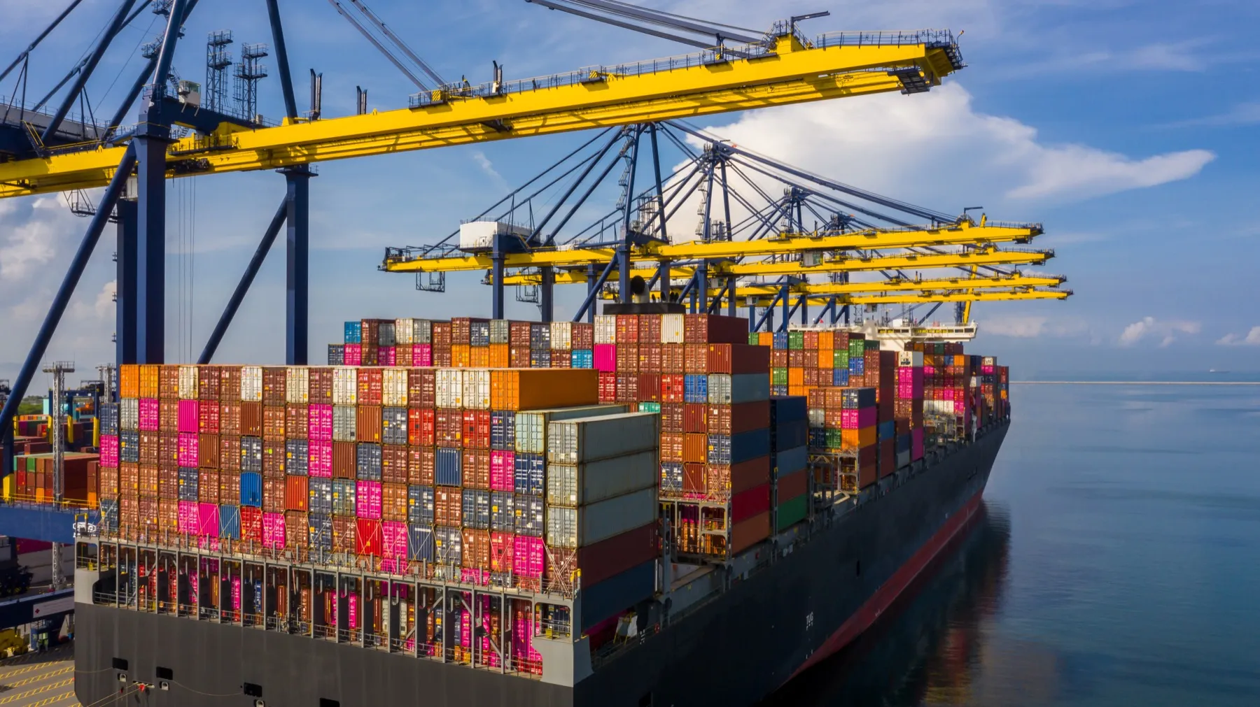 A container ship alongside the quay cranes at a port on a sunny day