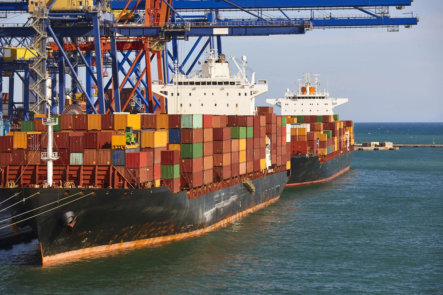 Container ships alongside the quay cranes under a blue sky